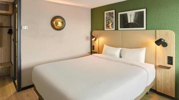 A modern hotel room with a large bed, a wooden headboard, two wall-mounted lamps, and two framed pictures above the bed. - Campanile NATURE - Saint-Germain-en-Laye (Saint-Germain-en-Laye)