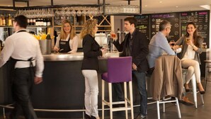 A bar area with a bartender, several patrons, and a modern interior with a curved counter and hanging glasses. - Campanile NATURE - Saint-Germain-en-Laye (Saint-Germain-en-Laye)