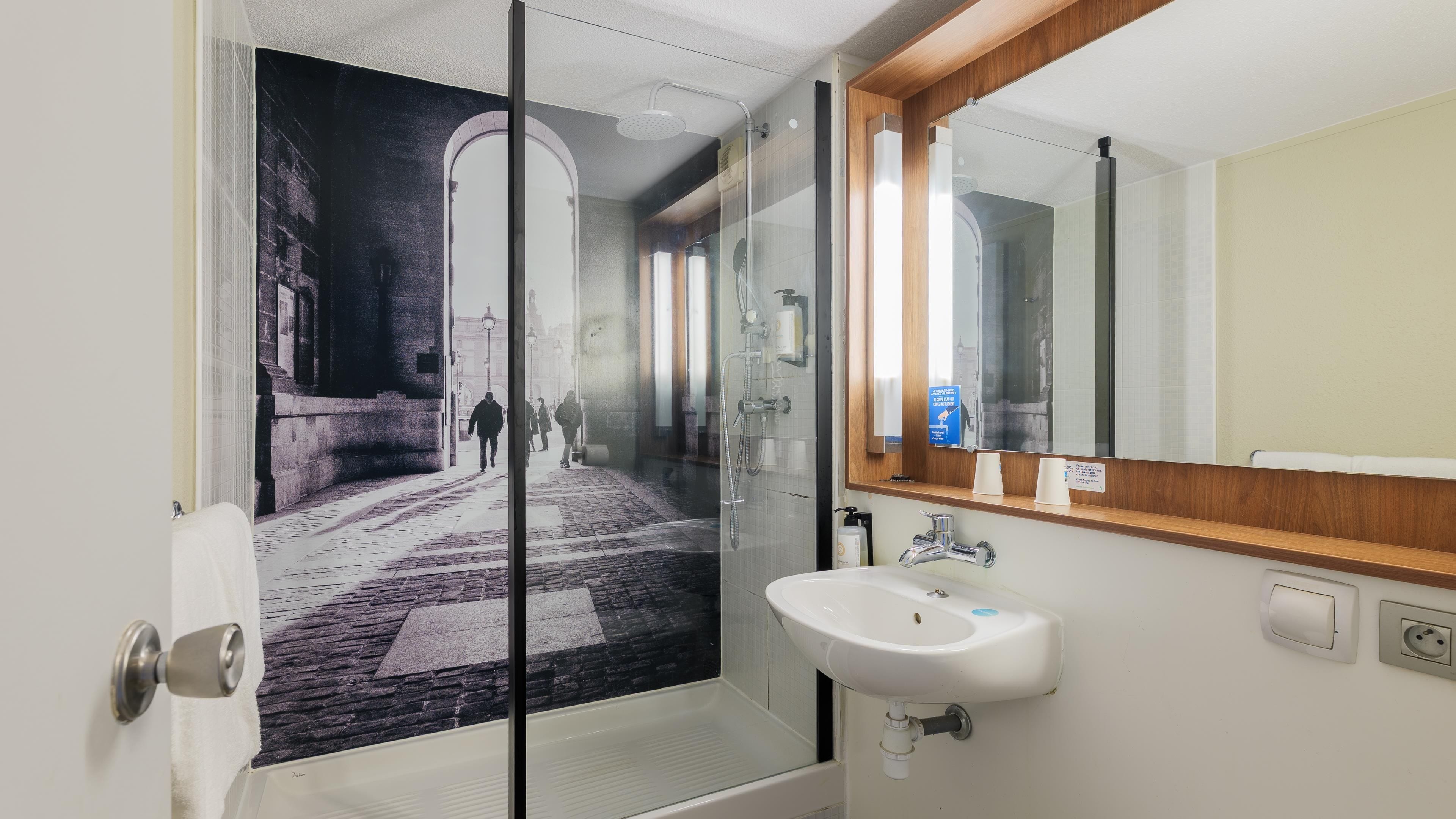Un bagno con box doccia in vetro, lavandino e specchio.