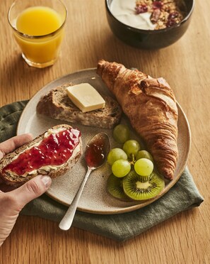 A plate with a croissant, a slice of bread with jam, grapes, kiwi slices, and a spoon. - Campanile NATURE - Saint-Germain-en-Laye (Saint-Germain-en-Laye)