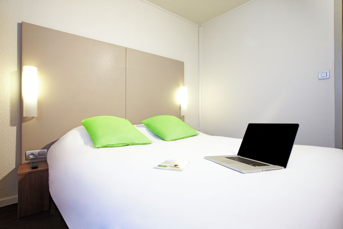 A neatly made bed with a laptop, pillows, and a remote control on a bedside table.