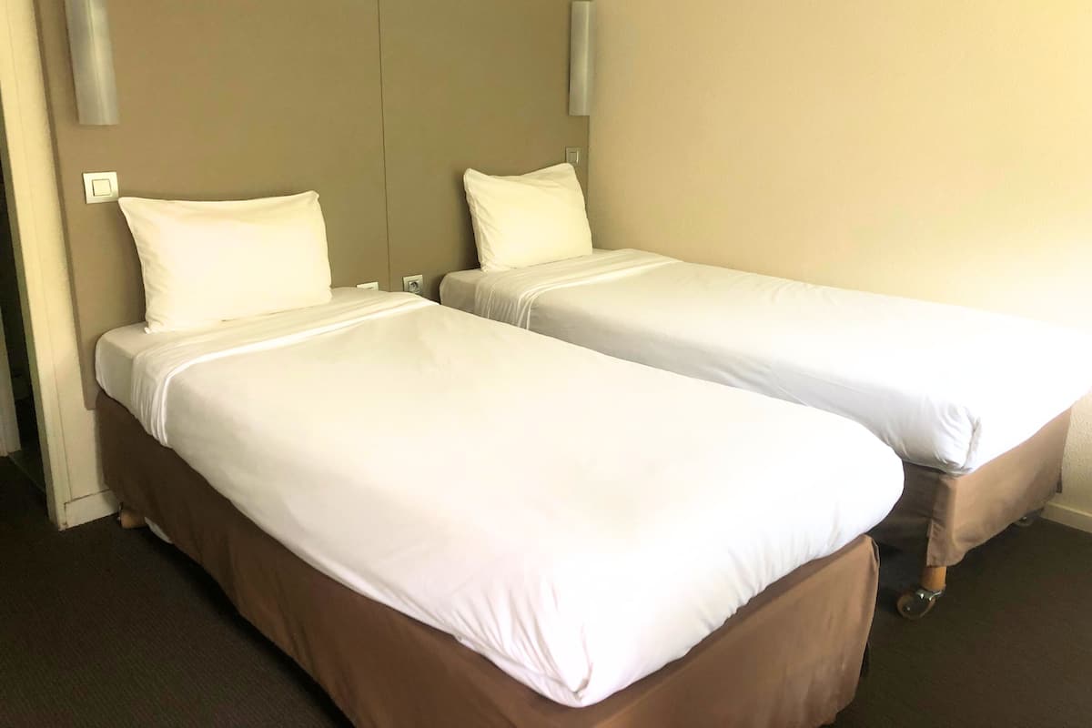 A hotel room with two single beds, each with a white mattress and matching pillows.