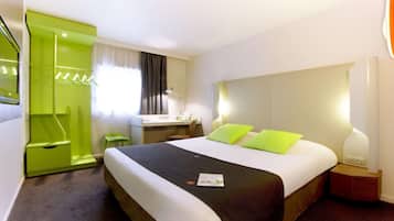 Quarto de hotel com cama, mesa de cabeceira, abajur e uma cadeira verde.