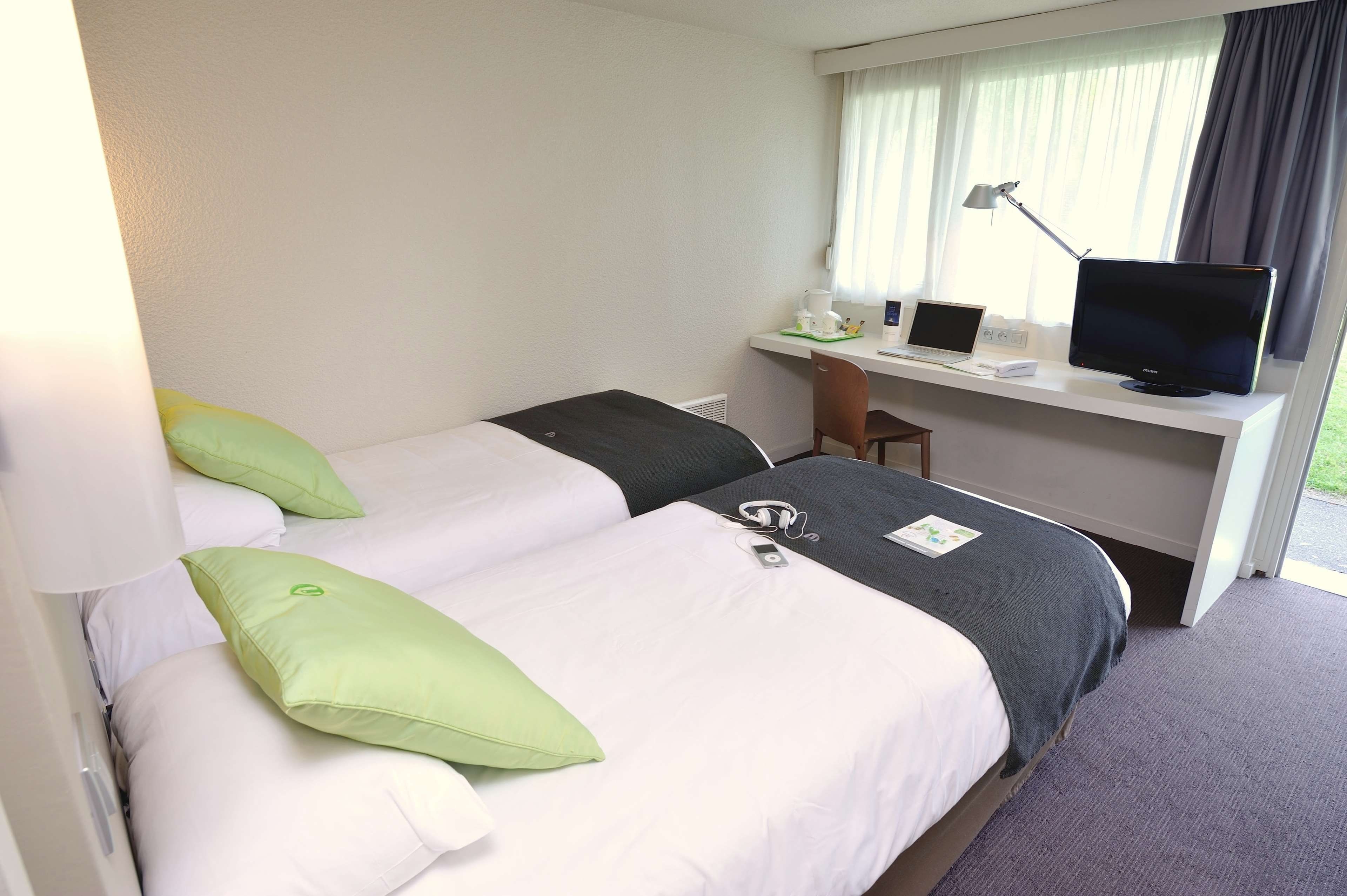 A hotel room with two beds, a desk with a computer and a television, and a window with curtains.
