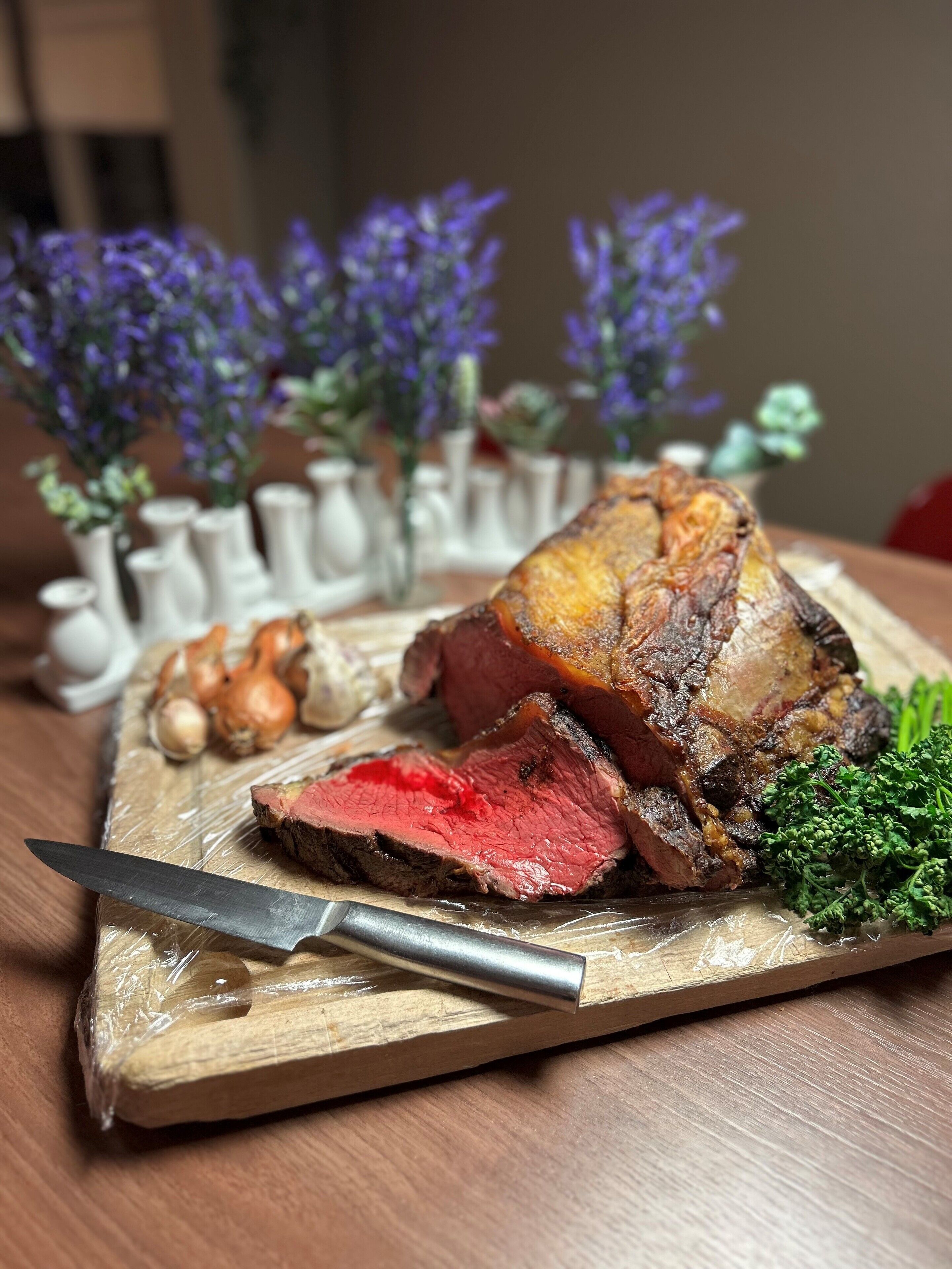 Une planche à découper en bois sur laquelle on a posé des tranches de rôti de bœuf, un couteau et quelques herbes aromatiques.