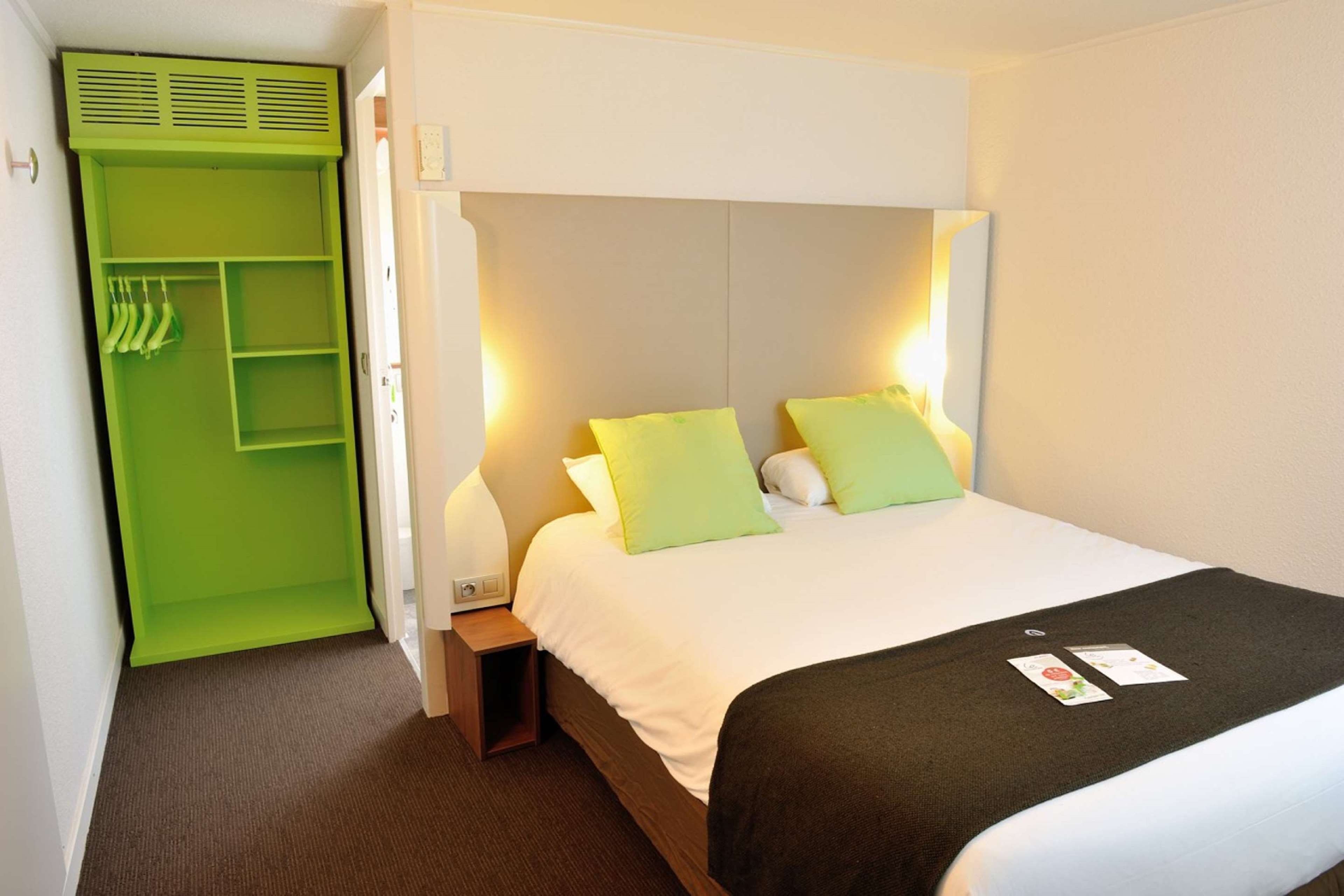 Una habitación de hotel con una cama, una mesita de noche y un armario verde.