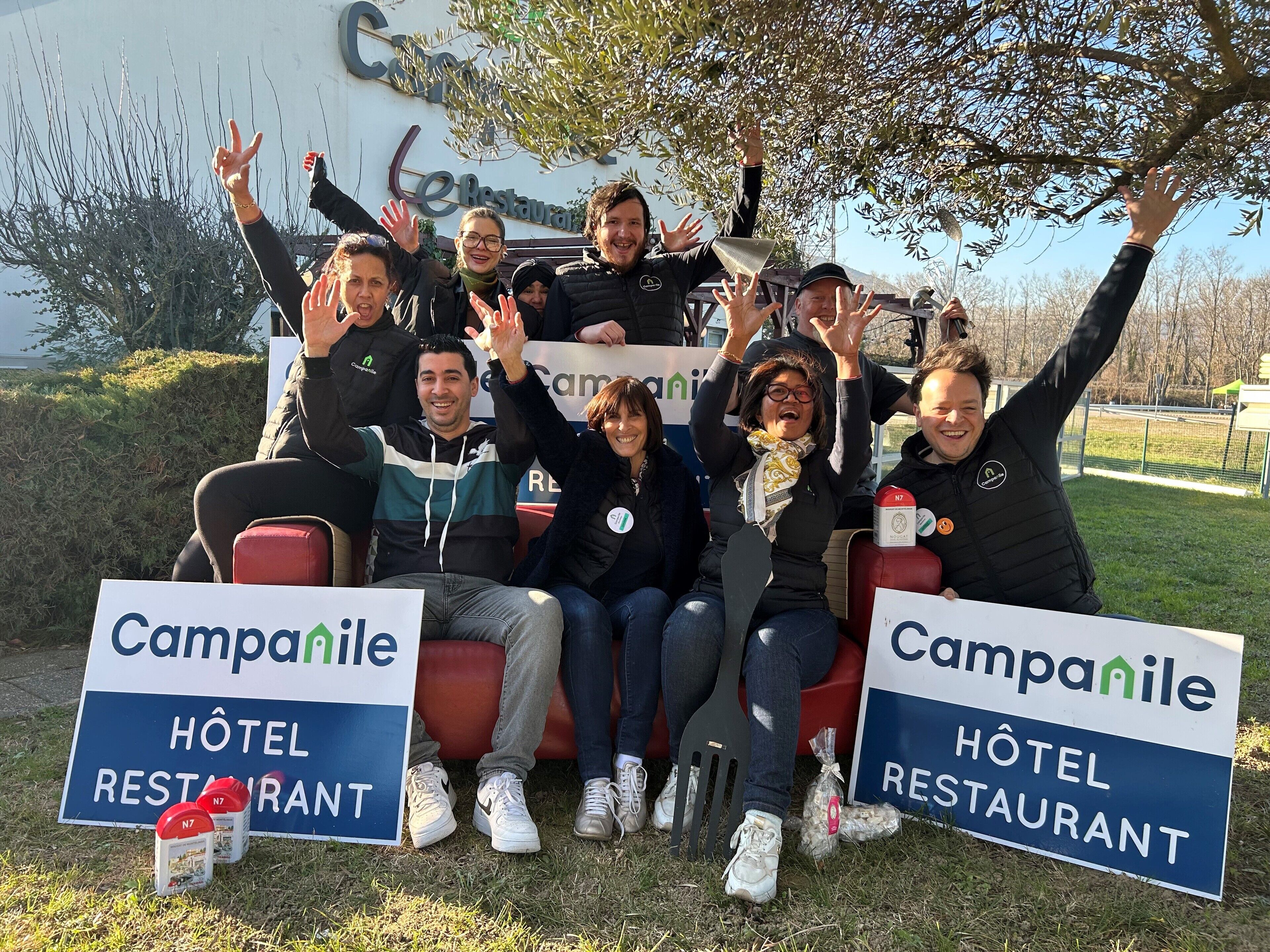 A group of people seated outdoors with signs for Campanile Hotel Restaurant in the background.