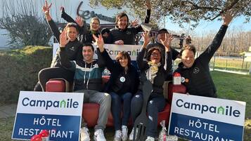 A group of people seated outdoors with signs for Campanile Hotel Restaurant in the background.