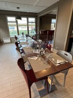 Un comedor con una mesa larga preparada para una comida, sillas y vistas al exterior.