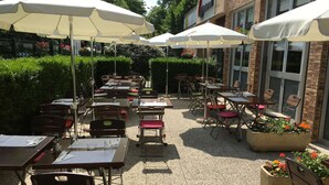 An outdoor patio with tables and chairs, umbrellas, and potted plants. - Campanile PRIME - Nanterre La Défense (Nanterre)