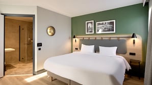 A modern hotel room with a large bed, a shower area, and two framed pictures on the wall. - Campanile PRIME - Nanterre La Défense (Nanterre)
