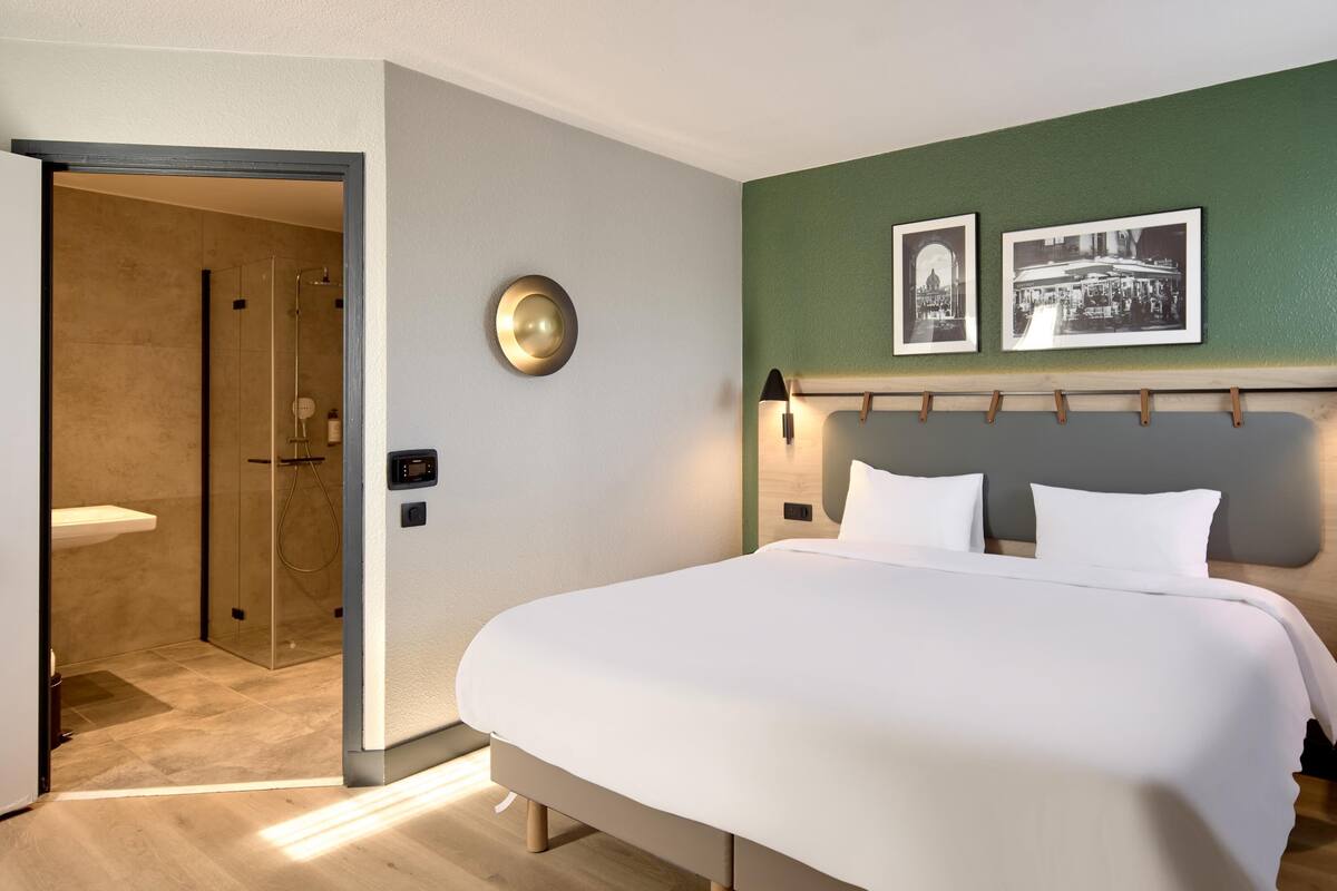 A modern hotel room with a large bed, a shower area, and two framed pictures on the wall.
