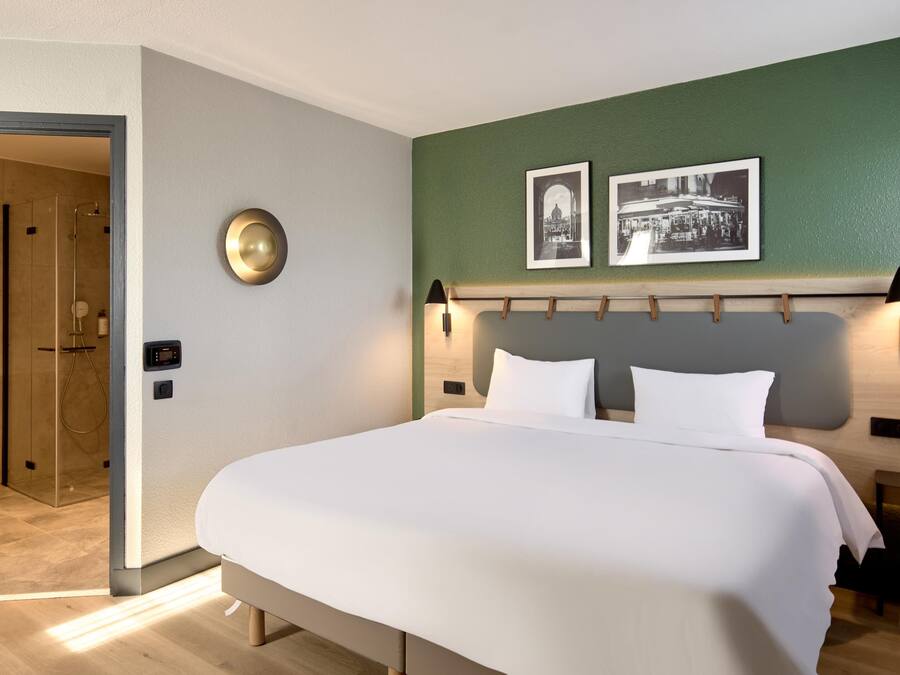A modern hotel room with a large bed, a shower area, and two framed pictures on the wall.