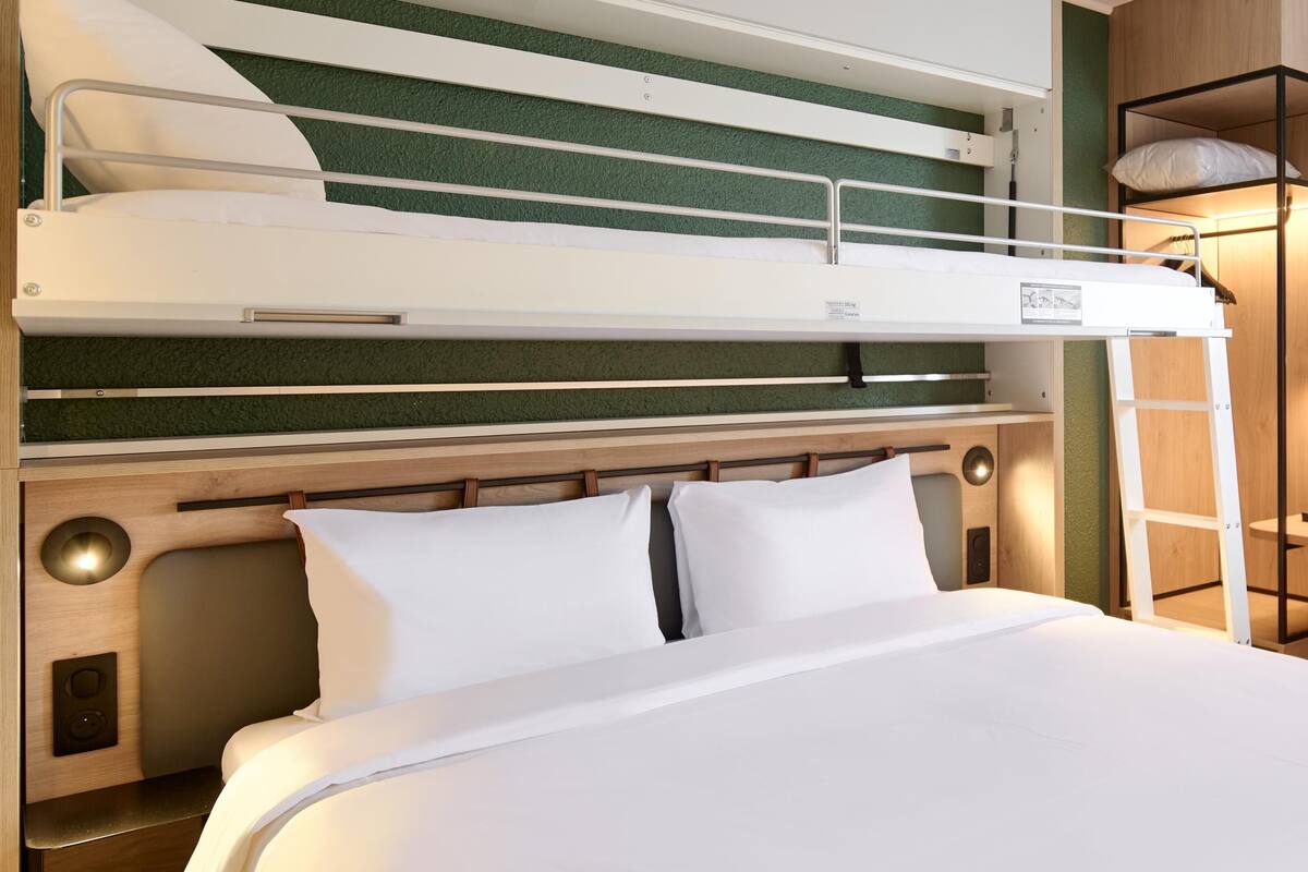 A bunk bed with a wooden headboard, a bedside table with a lamp, and a small shelf with a pillow.