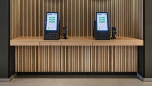 A self-checkin area with two kiosks, a wooden slat wall, and a dark floor. - Campanile PRIME - Nanterre La Défense (Nanterre)