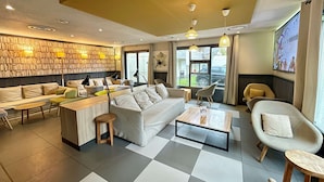 A modern living room with a sofa, coffee table, and chairs, a bookshelf wall, and a TV mounted on the wall.