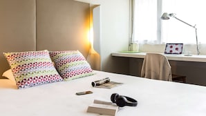 A neatly made bed with patterned pillows, a bedside table with a lamp, a laptop, and a chair.
