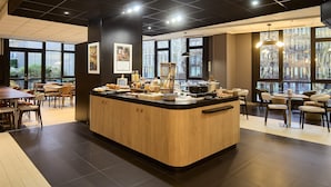 A modern cafe with a central wooden counter, large windows, and a mix of seating arrangements. - Campanile PRIME - Arcueil (Arcueil)