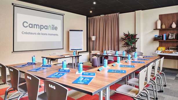 A conference room with a large screen displaying 'Campanile' and 'Créateurs de bons moments.' Tables are set with nameplates, water bottles, and blue name cards. - Campanile PRIME - Arcueil (Arcueil)