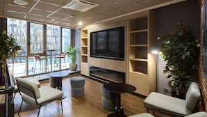 A modern lounge area with a large flat-screen TV, comfortable seating, and large windows offering a view of the city. - Campanile PRIME - Arcueil (Arcueil)