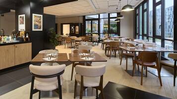 A modern restaurant with multiple dining tables and chairs, large windows, and a counter with various food items.