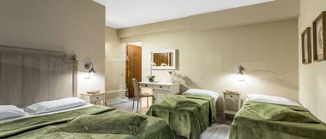 A hotel room with three beds, a desk, a chair, and a mirror.