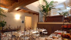 A dining area with tables and chairs, a balcony with plants, and a variety of food items on a stand. - Hotel Del Borgo (Bologna)