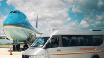 Un autobús estacionado en la plataforma de rodadura, con la nariz de un avión visible al fondo.