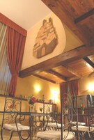 Een kamer met een rustiek houten plafond, een decoratief wandobject en metalen stoelen met witte kussens.