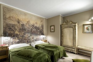 Een kamer met twee bedden, een groot wandtapijt, een kast en een lijst met een foto aan de muur.