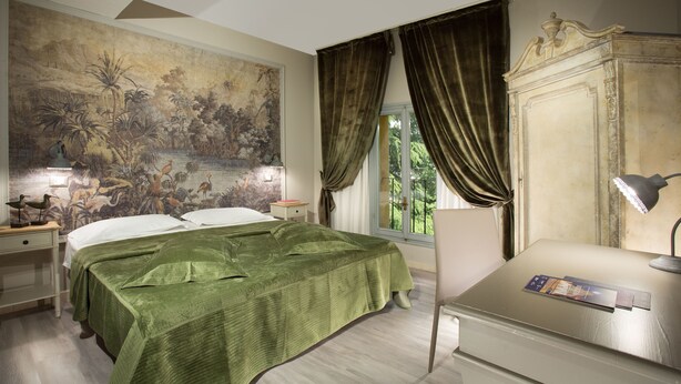 A bedroom with a large mural, a bed with green bedding, a nightstand, a dresser, and a window with curtains. - Hotel Del Borgo (Bologna)