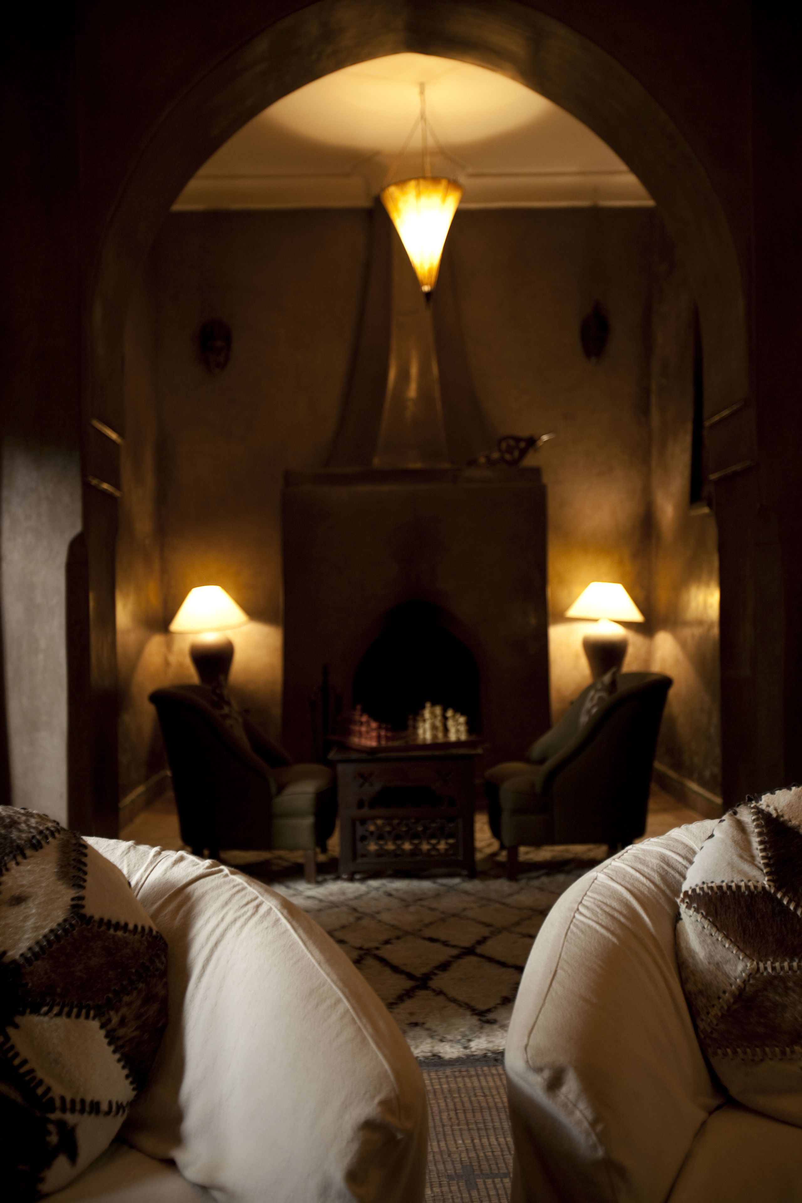 A dimly lit room with a fireplace, two armchairs, and a table.