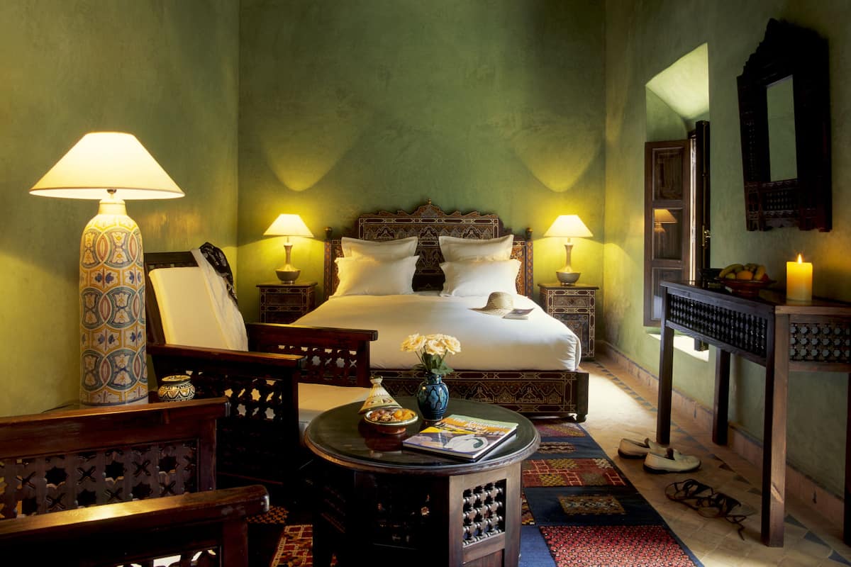 A bedroom with a bed, two bedside lamps, a nightstand with a lamp, a small table with a book and a vase, and a mirror on the wall.