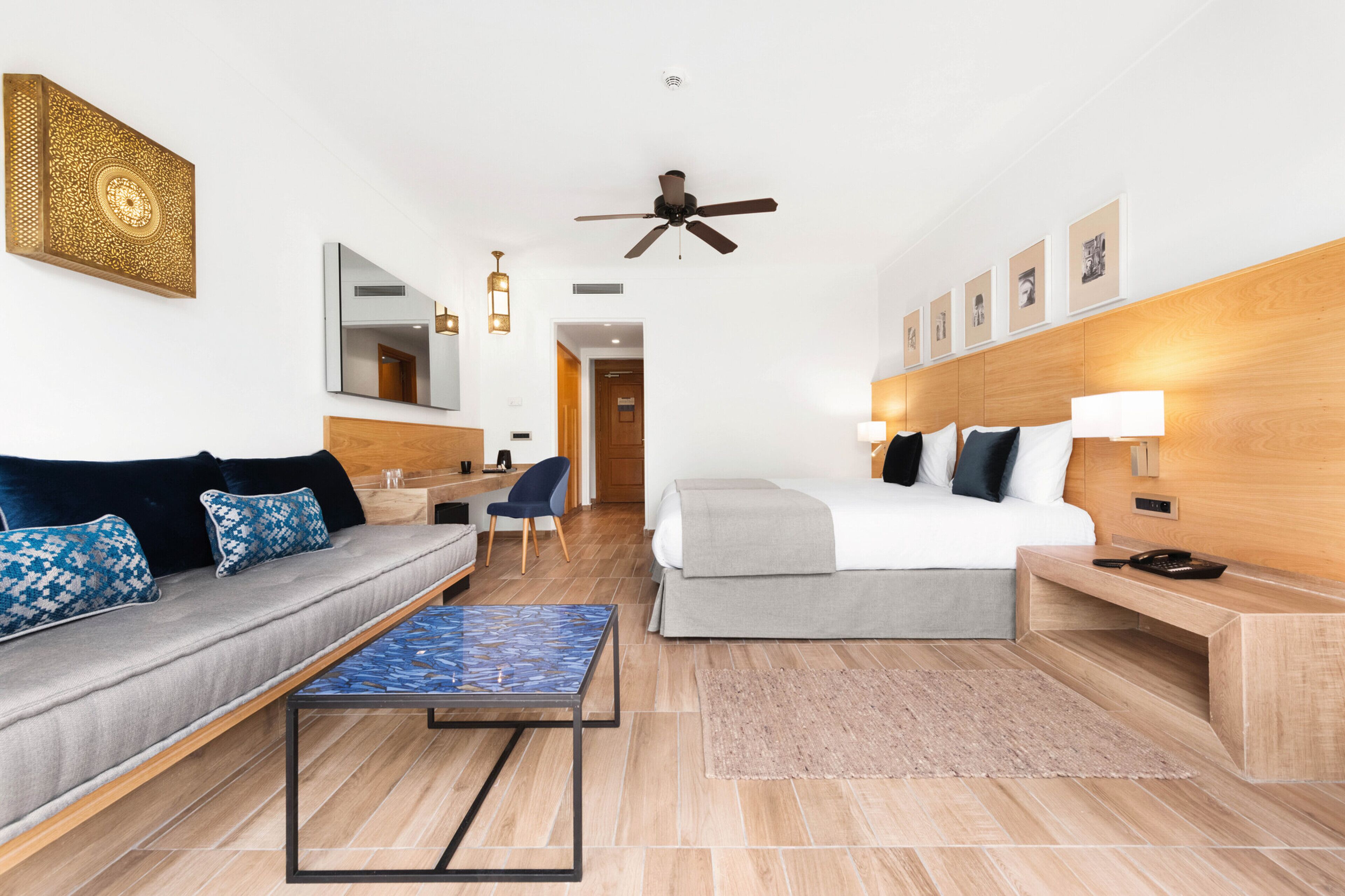 Ein modernes Hotelzimmer mit einer Couch, einem Bett, einem Schreibtisch und einem Deckenventilator.