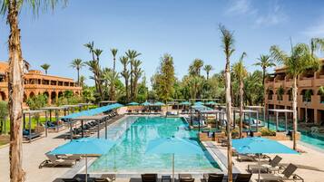 A pool area with sun loungers, umbrellas, and palm trees.