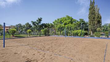 A sandy volleyball court with blue boundary lines, surrounded by trees and a fence.