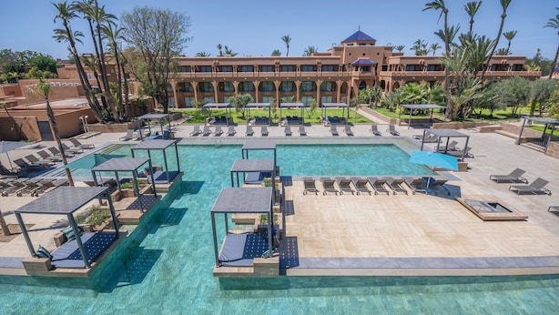 Un espace piscine d’un complexe hôtelier, avec des chaises longues, un toboggan aquatique et, au fond, un bâtiment doté de nombreux balcons.