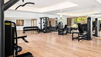 Une salle de sport moderne équipée de divers appareils d’exercice, dotée de grandes fenêtres et d’un plancher en bois.