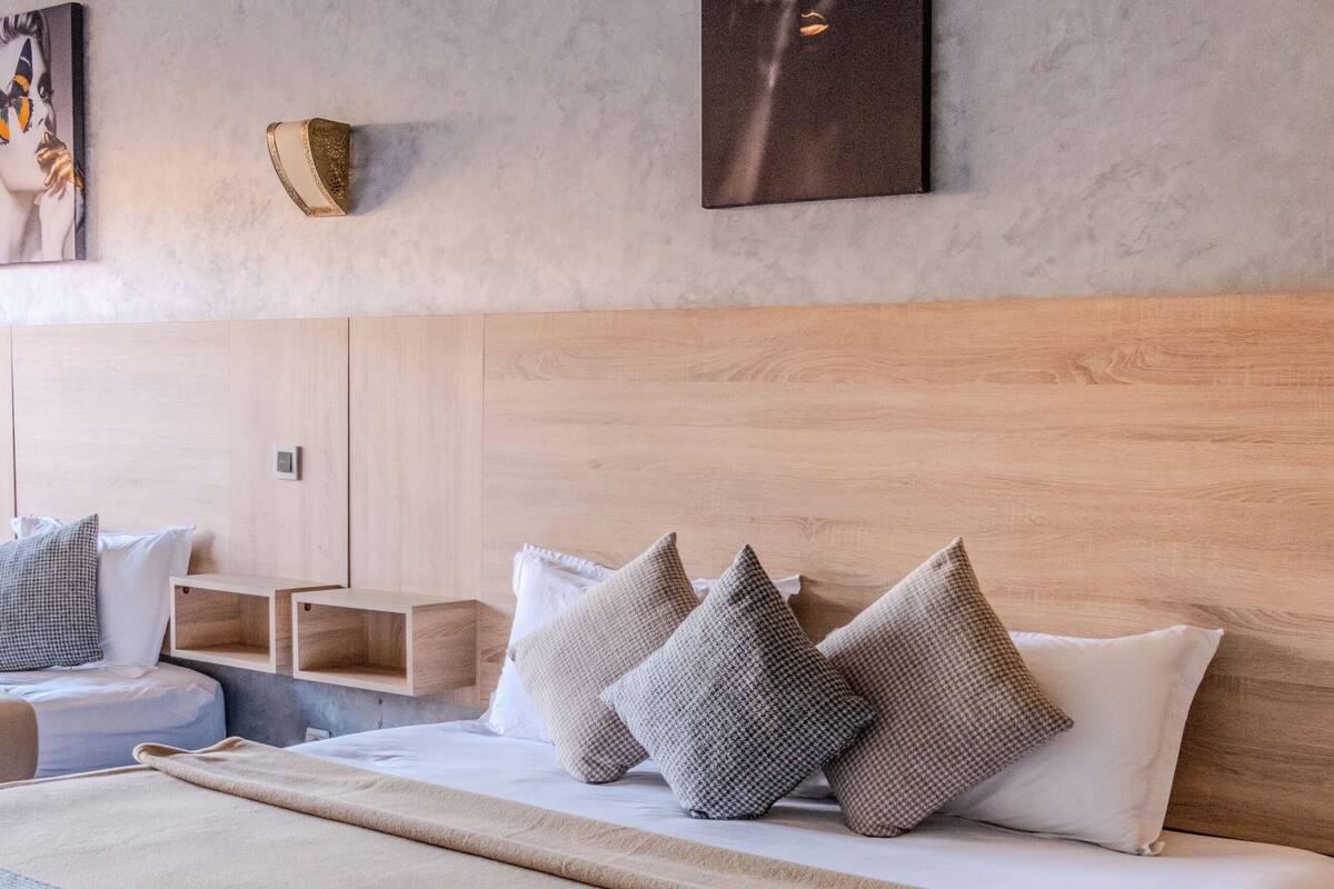A modern hotel room with a large bed, a bedside table, a nightstand, and a wall-mounted lamp.