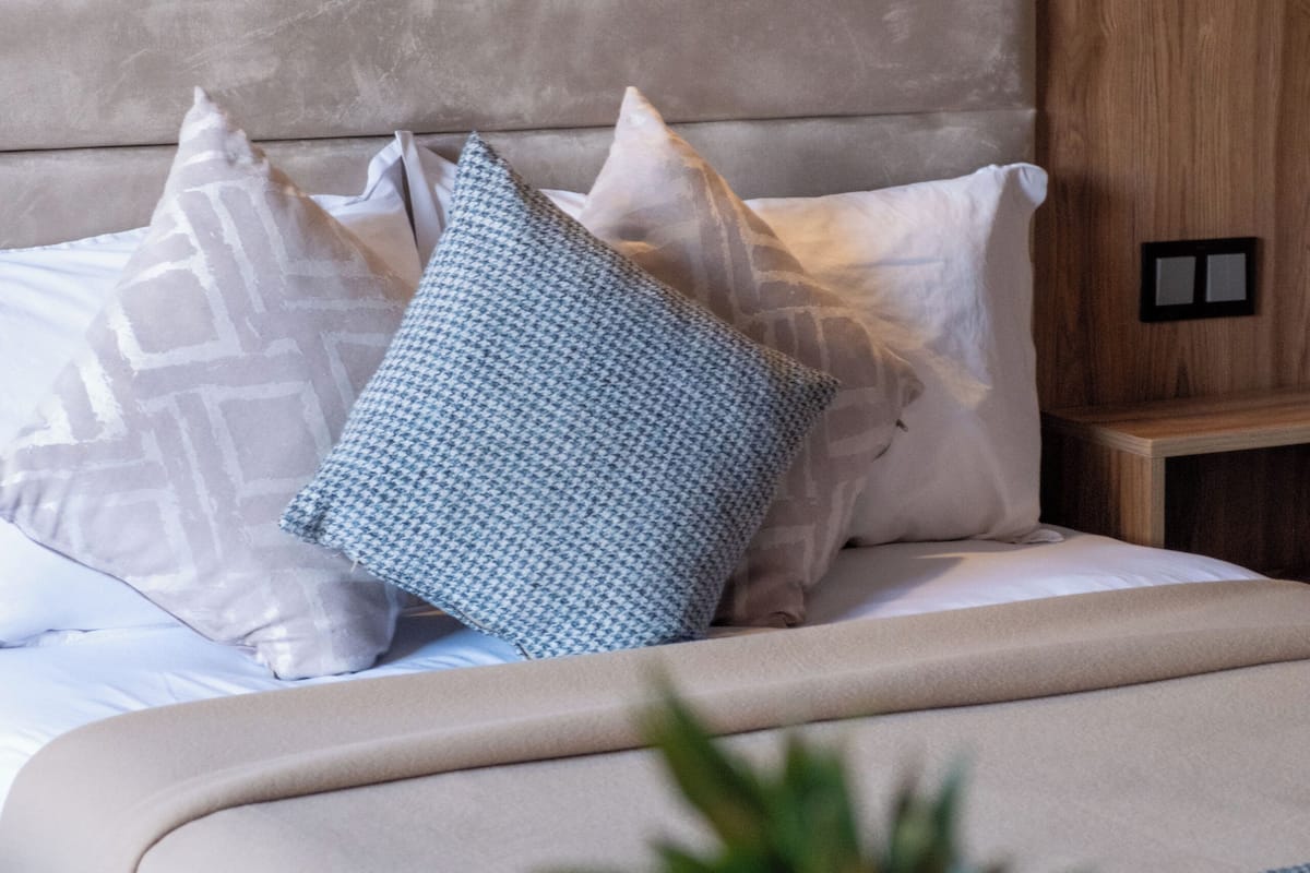 A bed with a wooden headboard, multiple pillows, and a bedside table with a small plant.