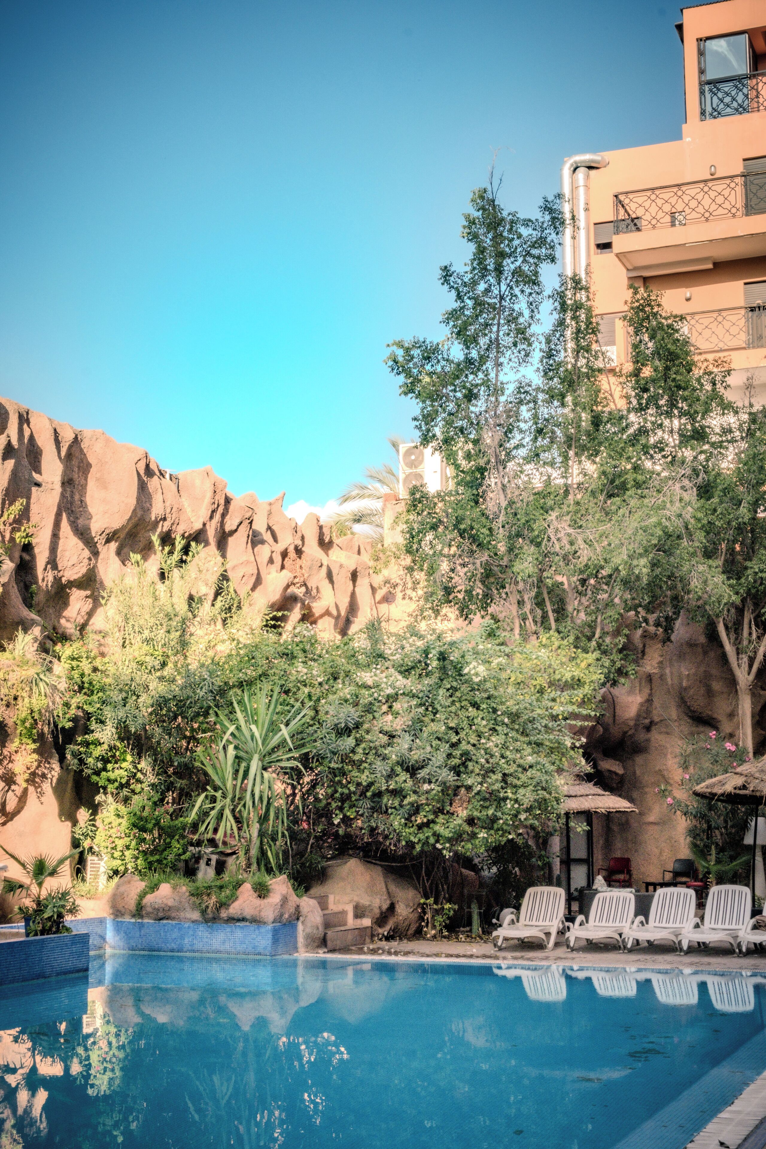 A swimming pool with lounge chairs, surrounded by greenery and a rocky backdrop.
