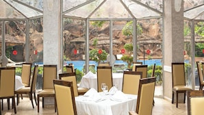 A restaurant with tables set for dining, large windows, and a view of a rocky landscape. - Imperial Holiday Hôtel & spa (Marrakech)