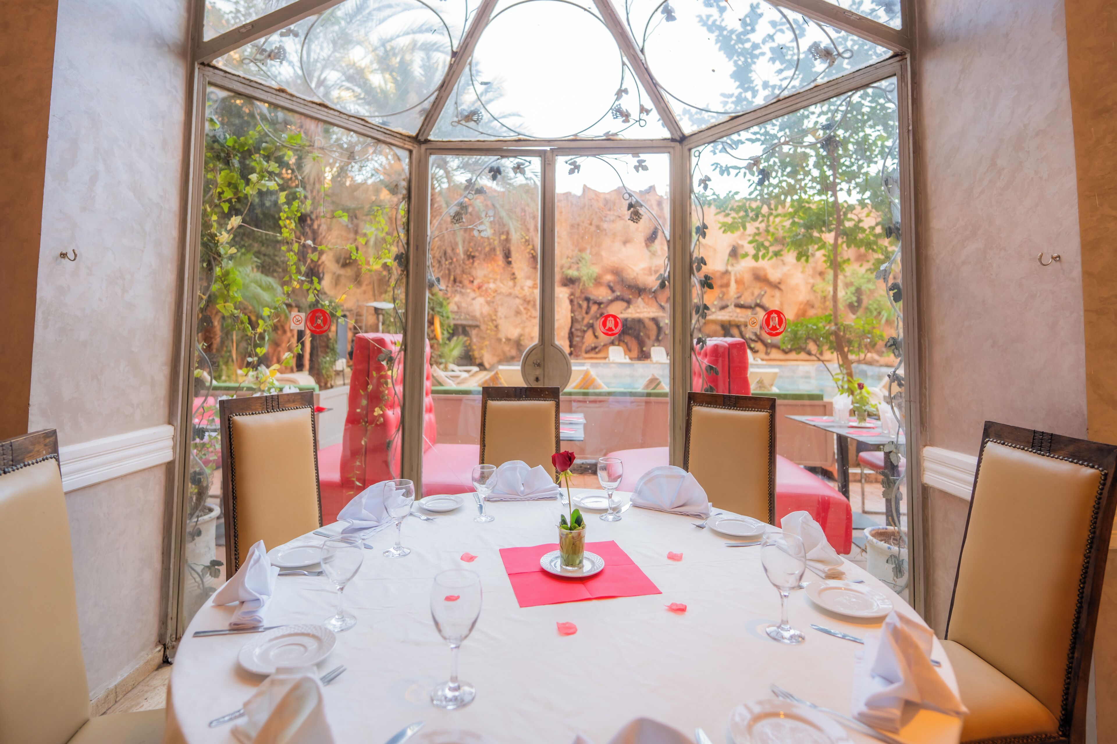 Un comedor con cerramiento de vidrio, mesas dispuestas con manteles blancos y sillas con tapicería color crema.