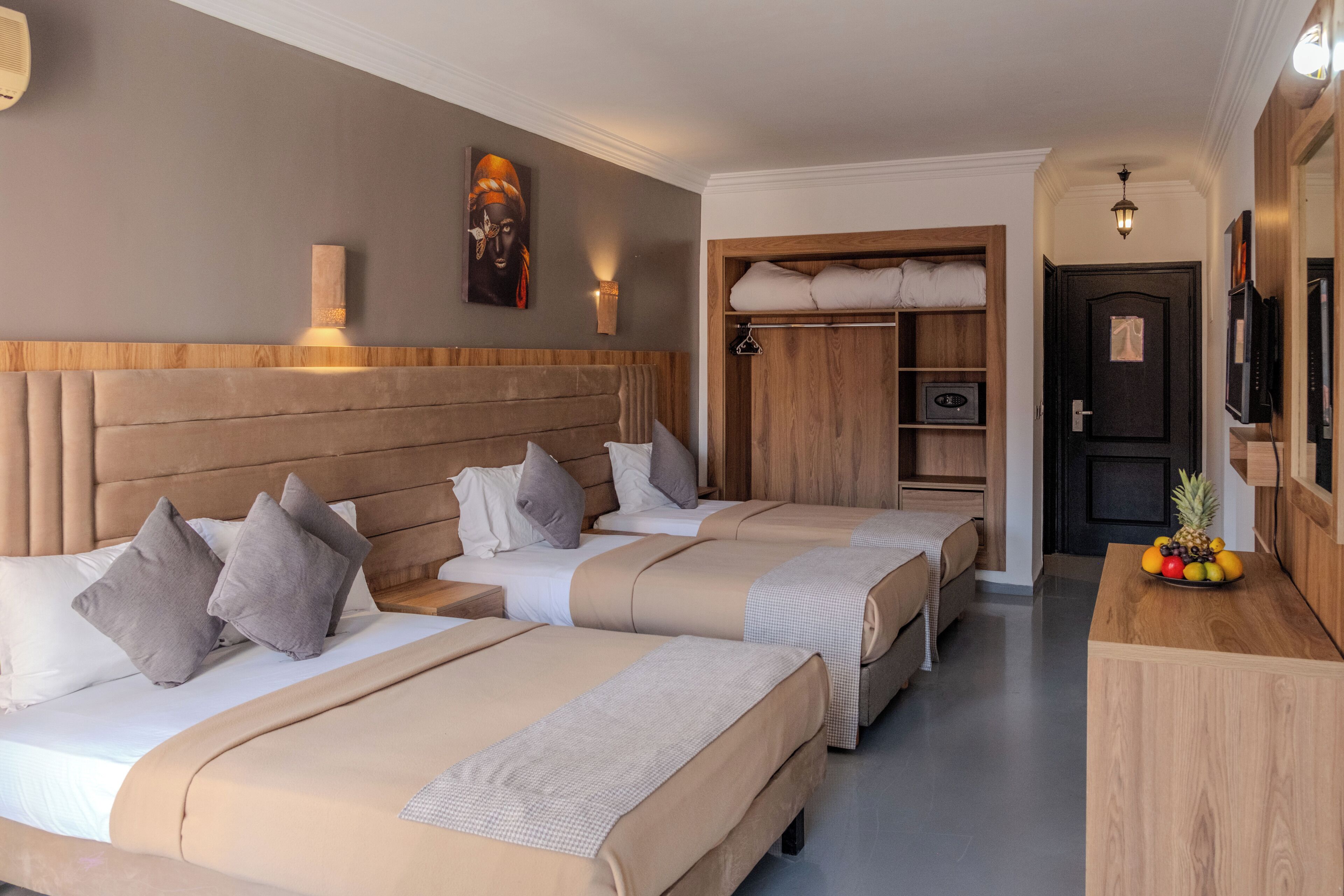 Habitació d'hotel amb tres llits, un panell frontal de fusta, un armari, un televisor i un plat de fruita.