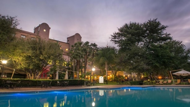 A hotel pool area with a clear view of the pool, lounge chairs, and surrounding trees. - Peermont Metcourt Inn at The Grand Palm Resort (Gaborone)