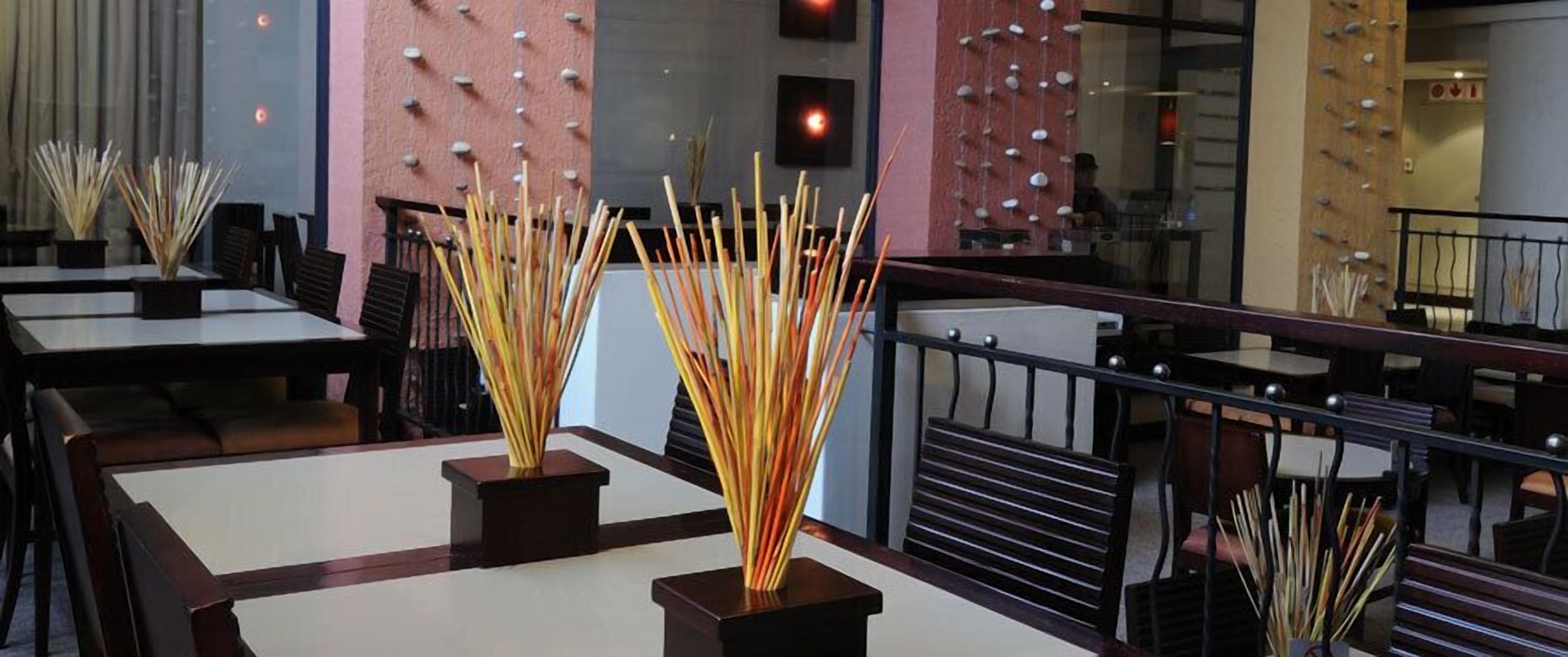 Een restaurantinterieur met tafels, stoelen en decoratieve bamboearrangementen.