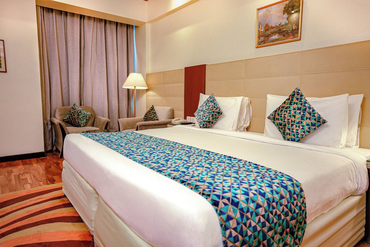 Una habitación de hotel con una cama grande, dos sillones, un escritorio, una lámpara y un cuadro en la pared.