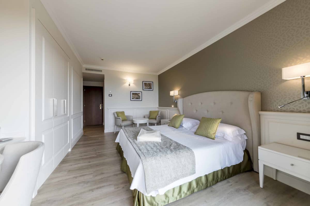 A hotel room with a large bed, a bedside table, a chair, and a desk.