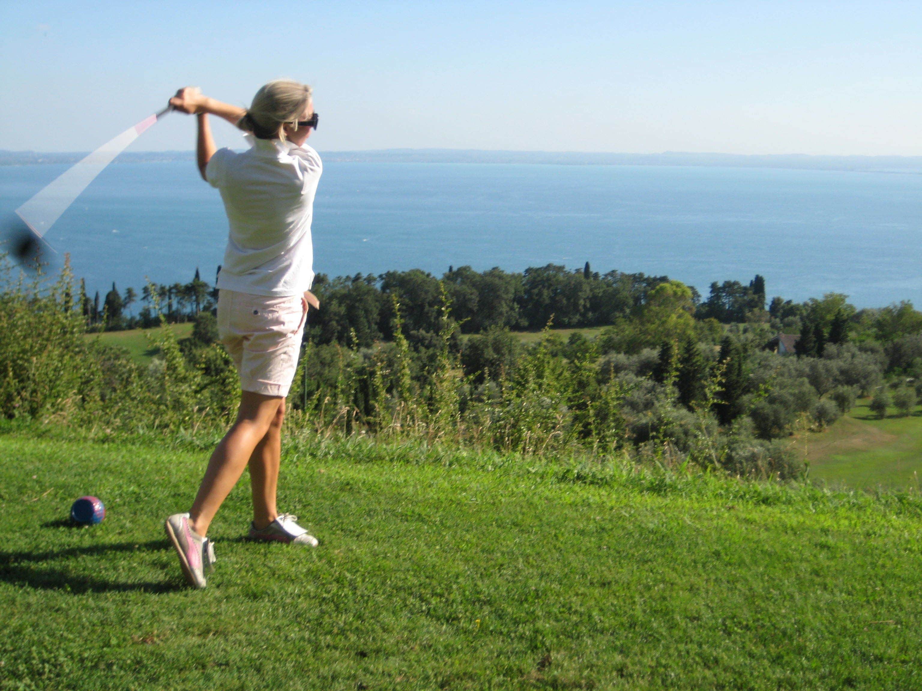 Eine Person spielt Golf auf einer grünen Wiese mit Blick auf das Meer.