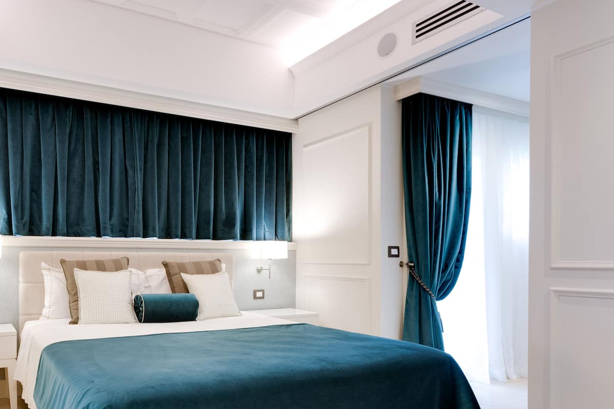 A modern bedroom with a large bed, white headboard, and dark blue curtains.